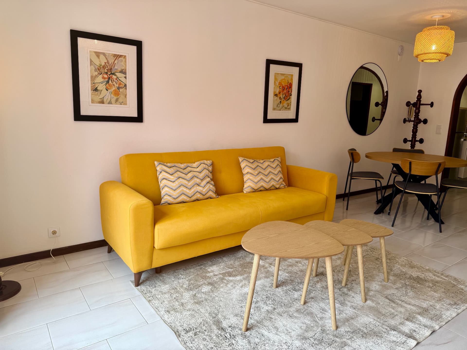 Close view of the Comfort Villa yellow sofa with chevron pillows, nesting tables and circular mirror