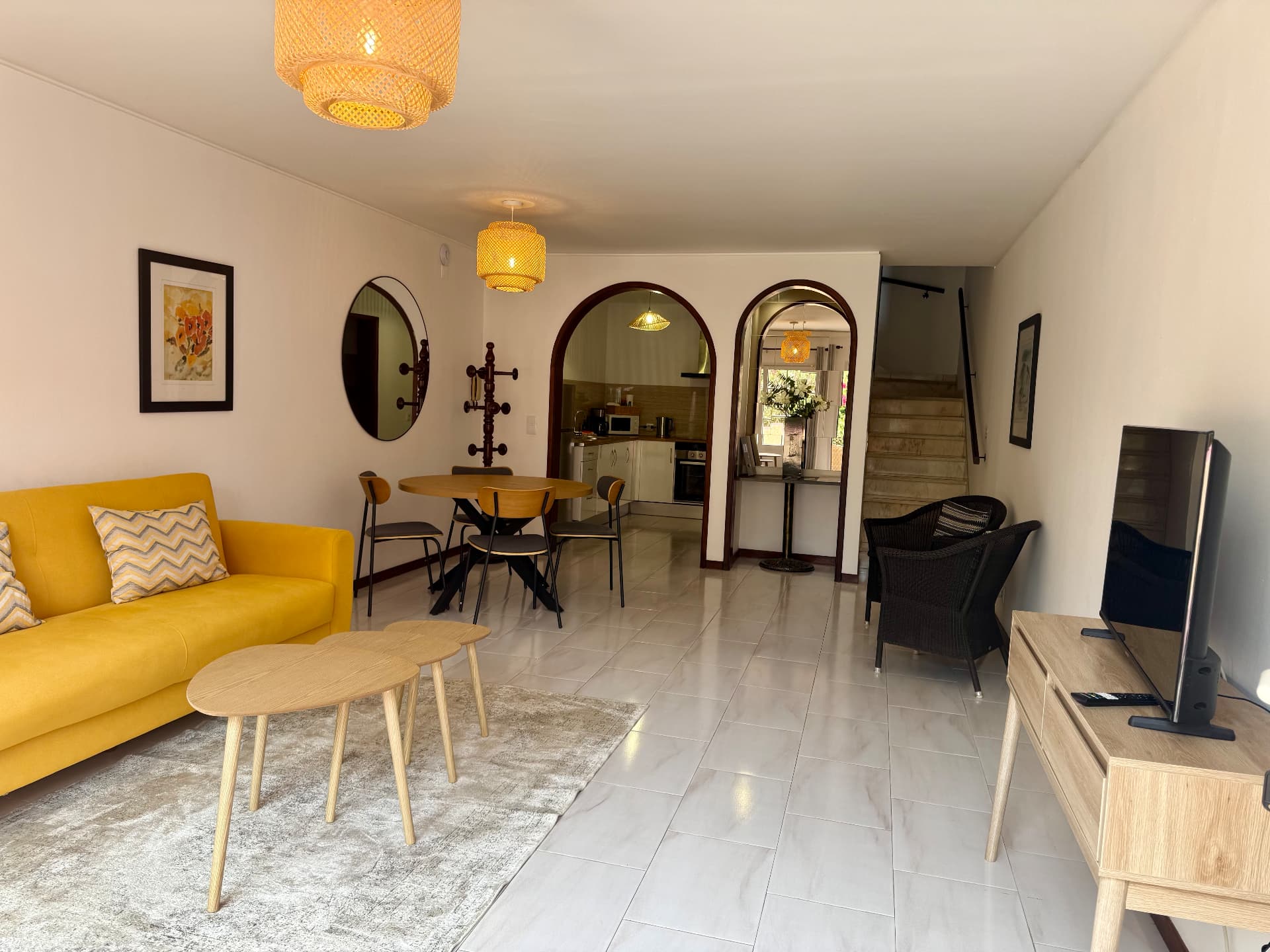 Wide view of a Comfort Villa living and dining room with TV console, yellow sofa and staircase